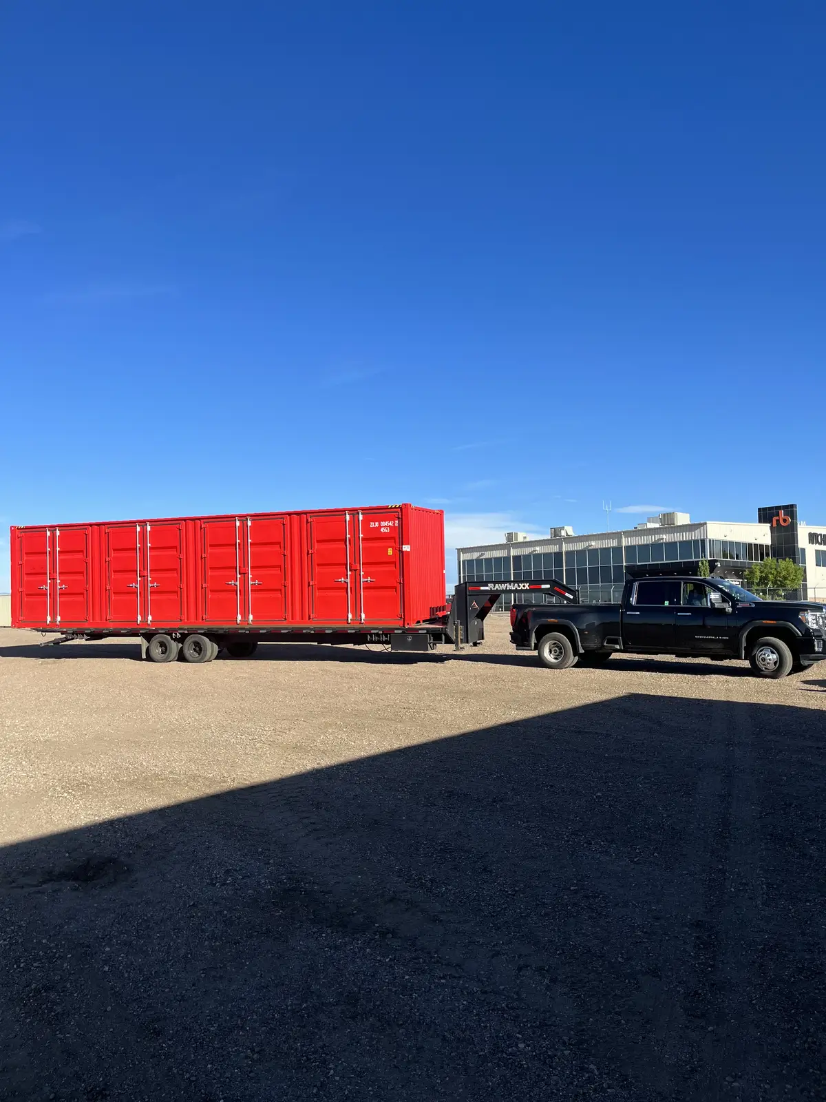 Bright red multi-door shipping container on a trailer behind a pickup