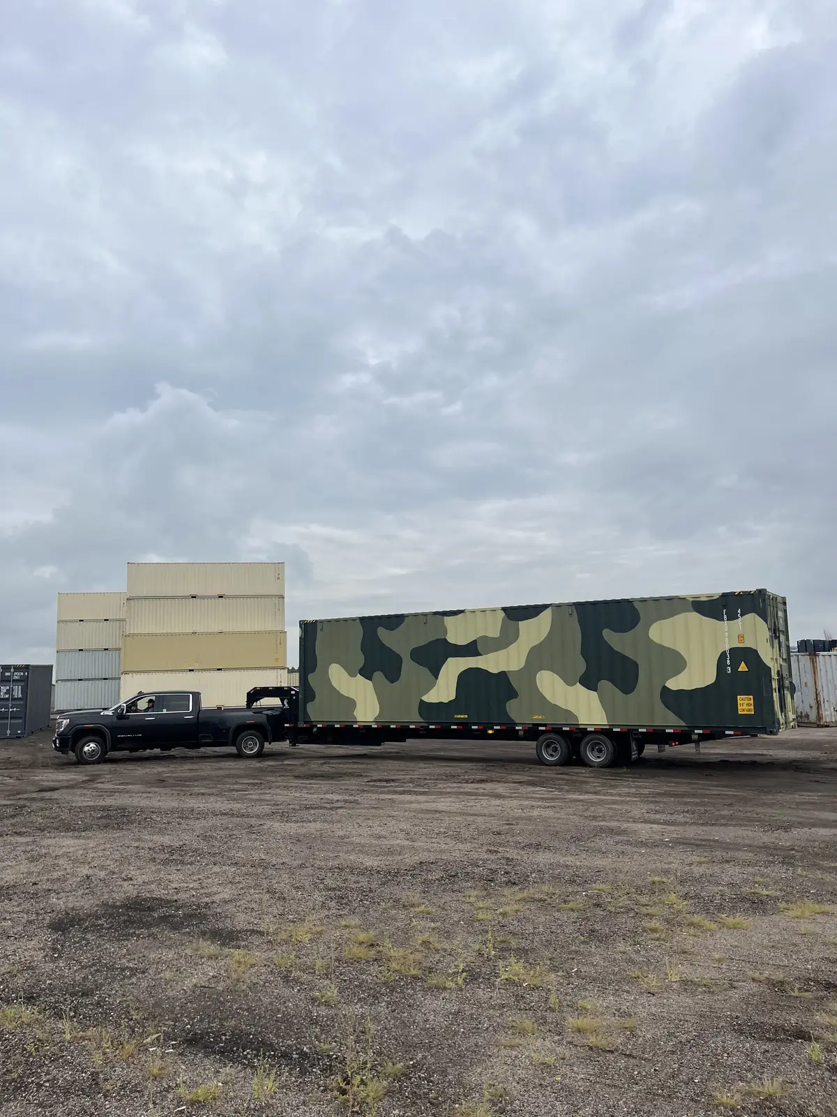 Shipping container painted in a green camouflage pattern on a flatbed trailer