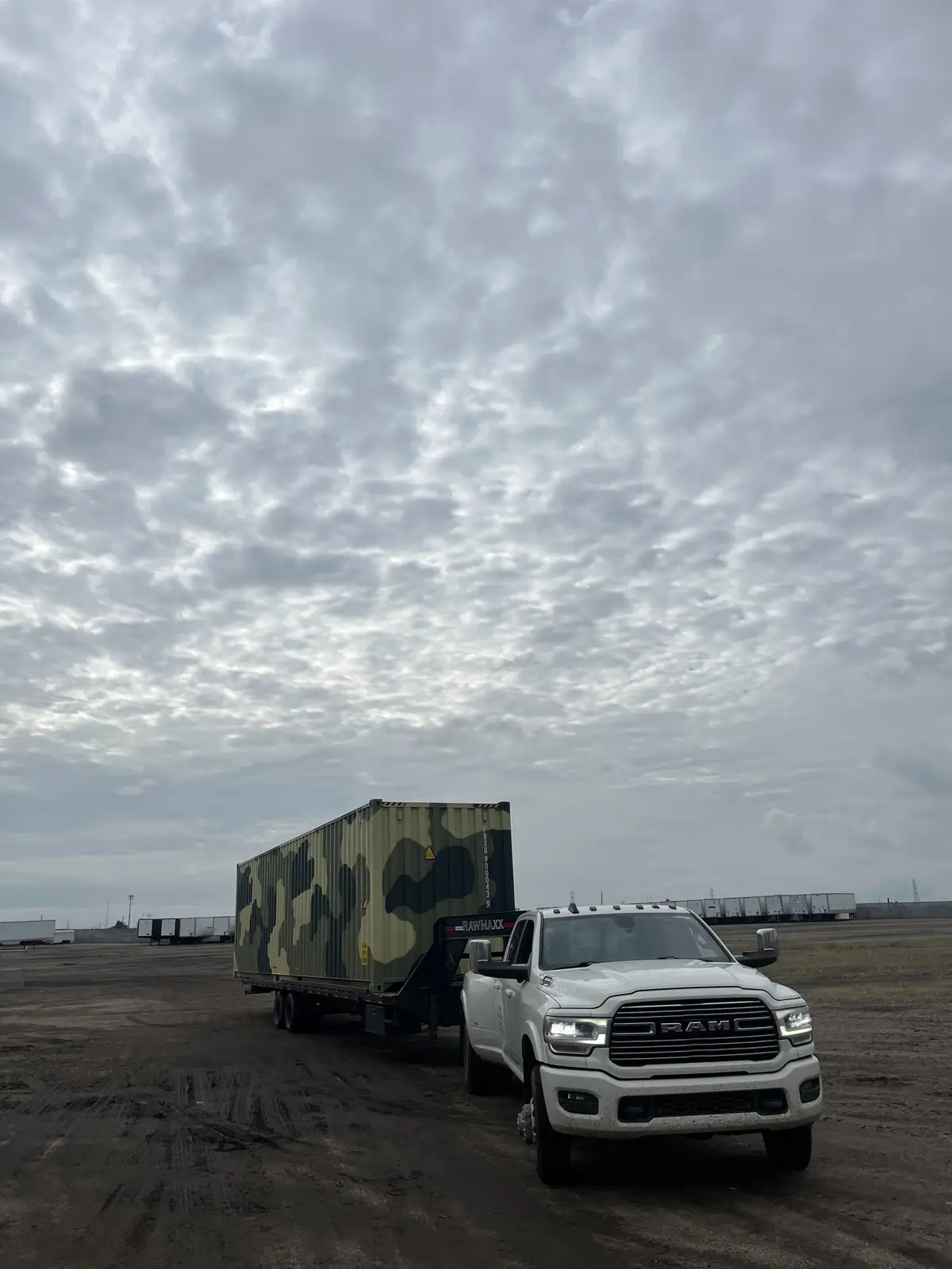 Camouflage-painted shipping container being towed by a white pickup truck