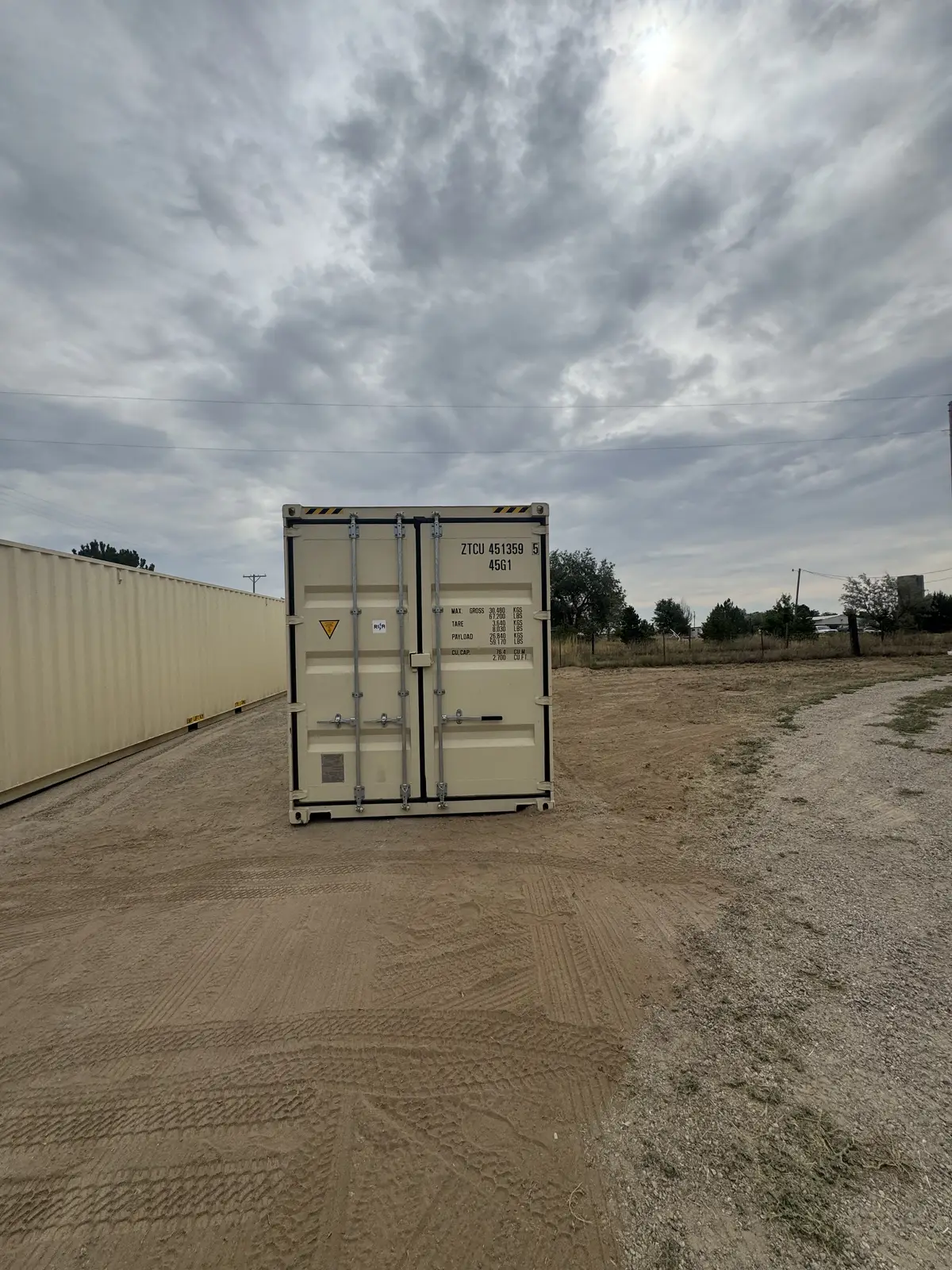 Front cargo doors of a tan shipping container on a dirt lot